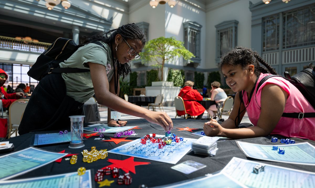 Two young girls engaging in a tabletop game during the "Gamers Universe" event at the Chicago Public Library, enjoying a fun and interactive gaming experience in a bright, open space.