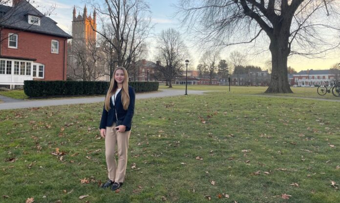 Reese Ratcliff, a graduate of Chicago City Day School, standing on a picturesque campus lawn with historic buildings and a church in the background during autumn.