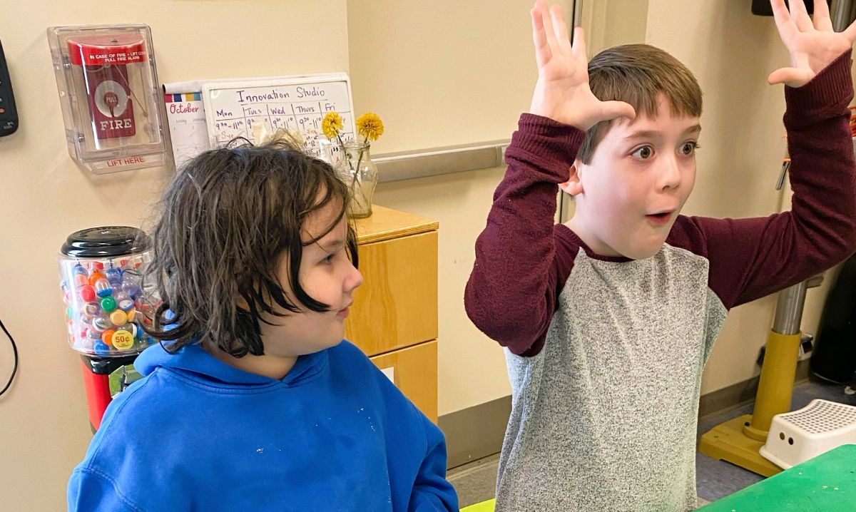 Two young students engaged in a creative classroom activity, with one child enthusiastically gesturing while sharing an idea, showcasing excitement and collaboration.