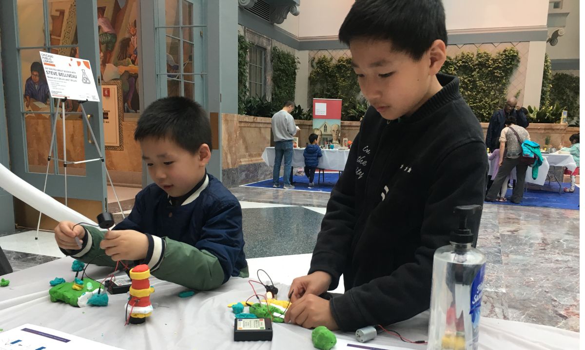 Two young boys participating in a hands-on STEAM activity during the Science Club's "STEAM-Powered Saturday" event at the Chicago Public Library, fostering creativity and learning in a collaborative environment.